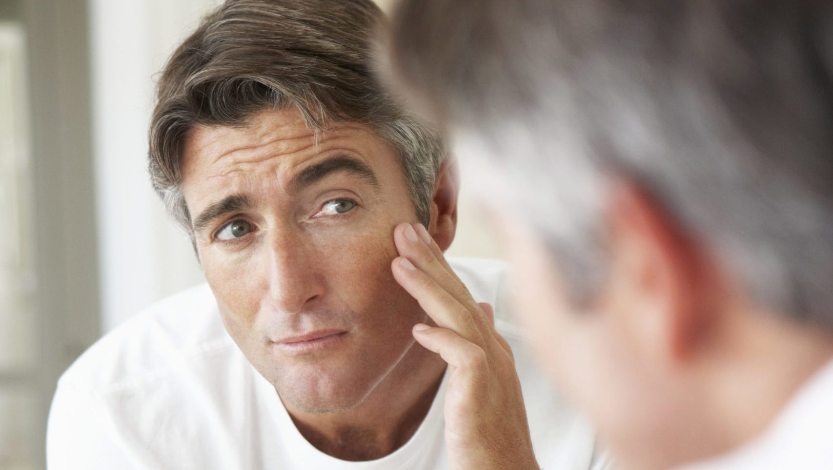 Man Looking At Reflection In Bathroom Mirror