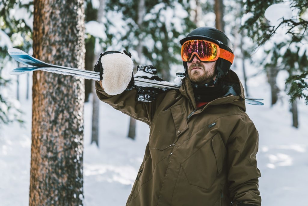 Man outside in the winter hiking with his skis over his shoulder; highlighting the importance of using sunscreen year round — even in winter.